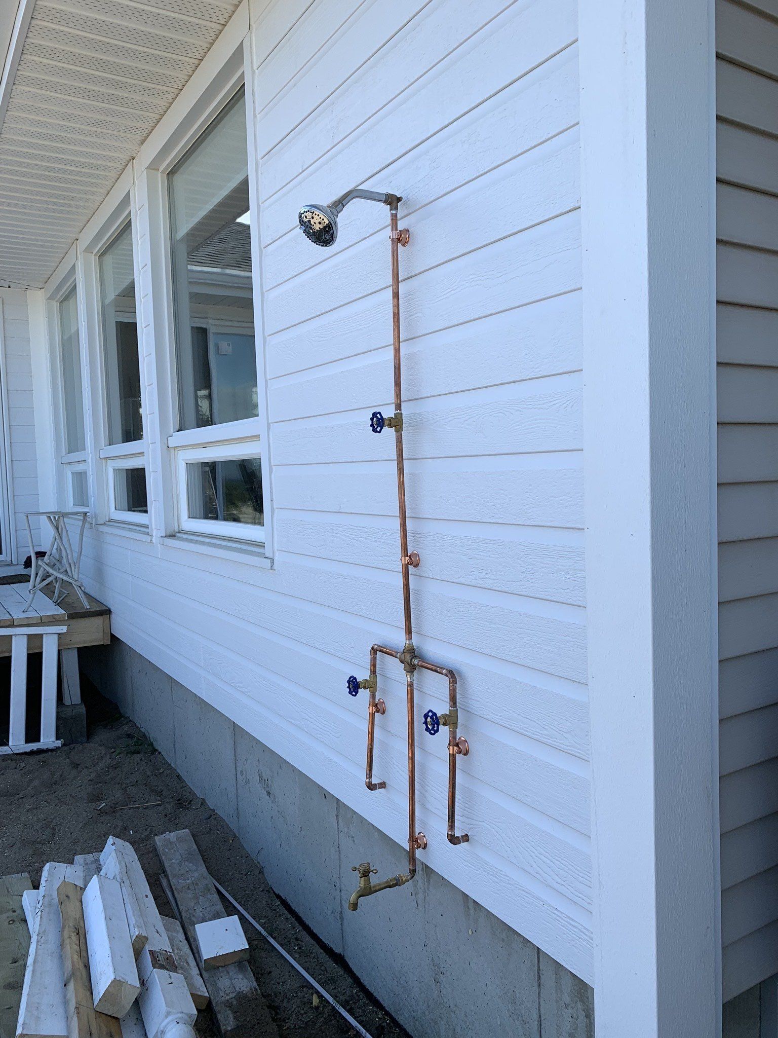 Outdoor copper shower on a white-sided house with two sets of spouts and a showerhead.