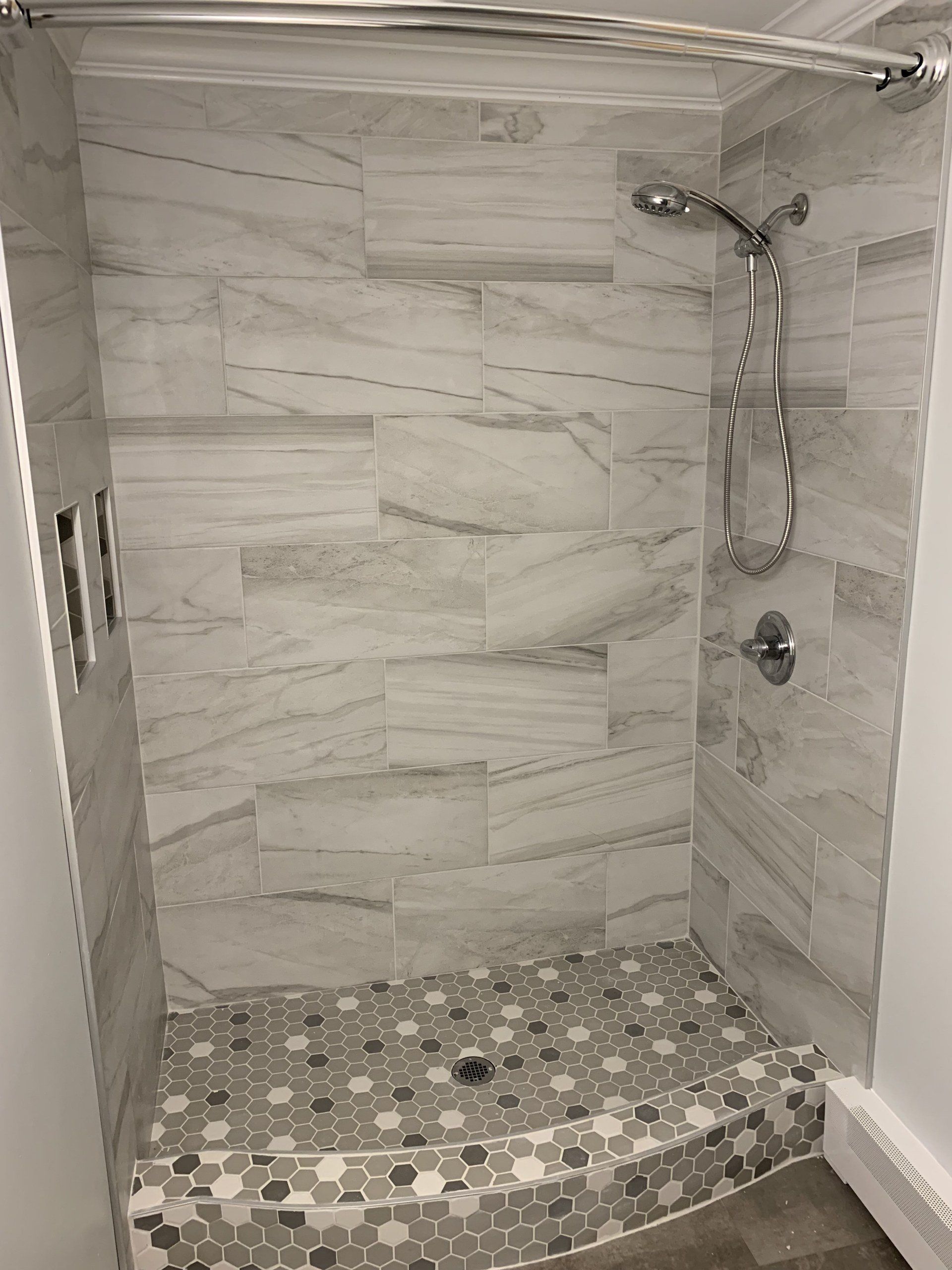 A newly tiled shower with gray and white marble-look tiles. A shower head and faucet are visible.