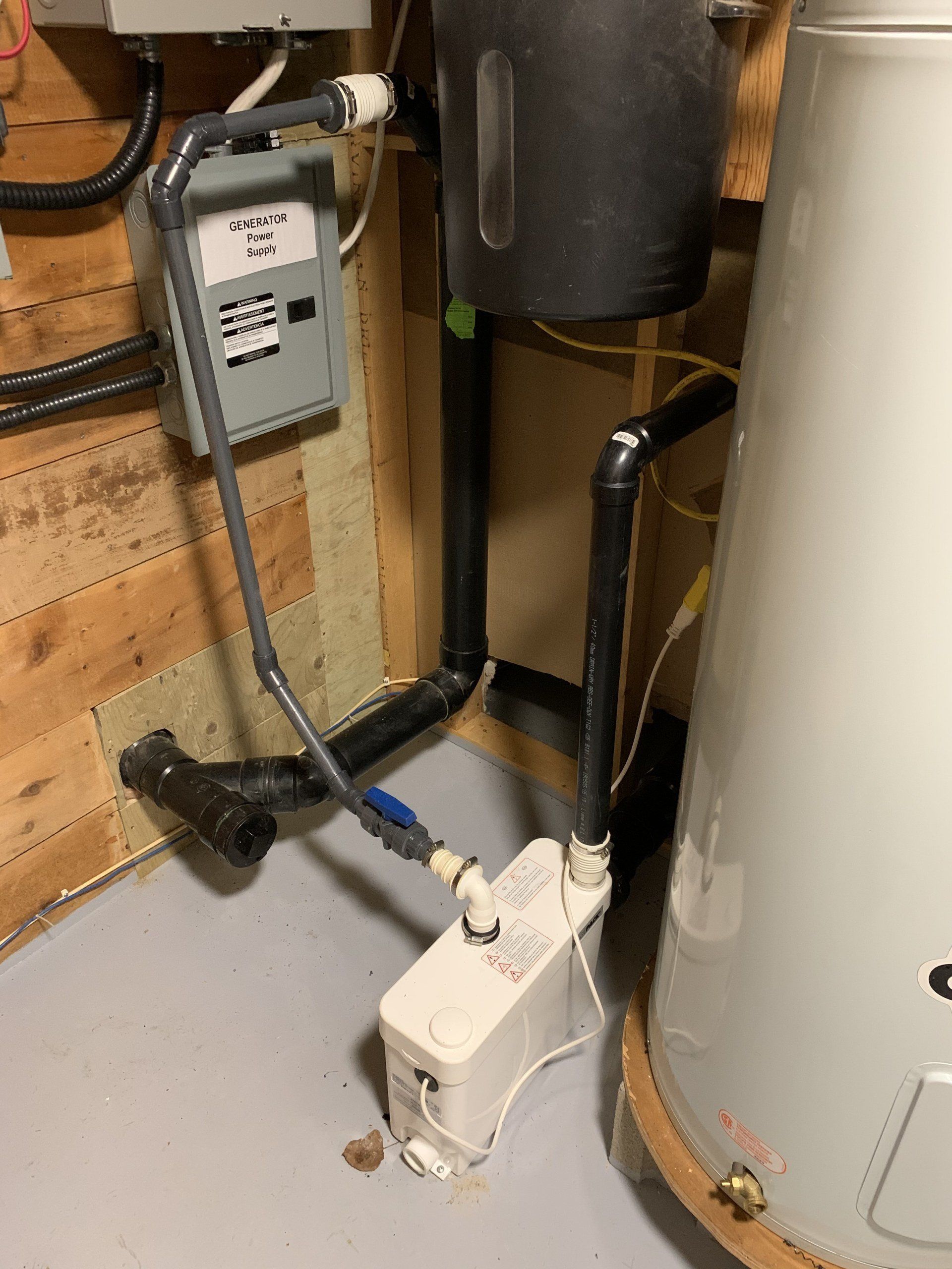 A water pump system with a gray box, black pipes, and a water heater in a basement.