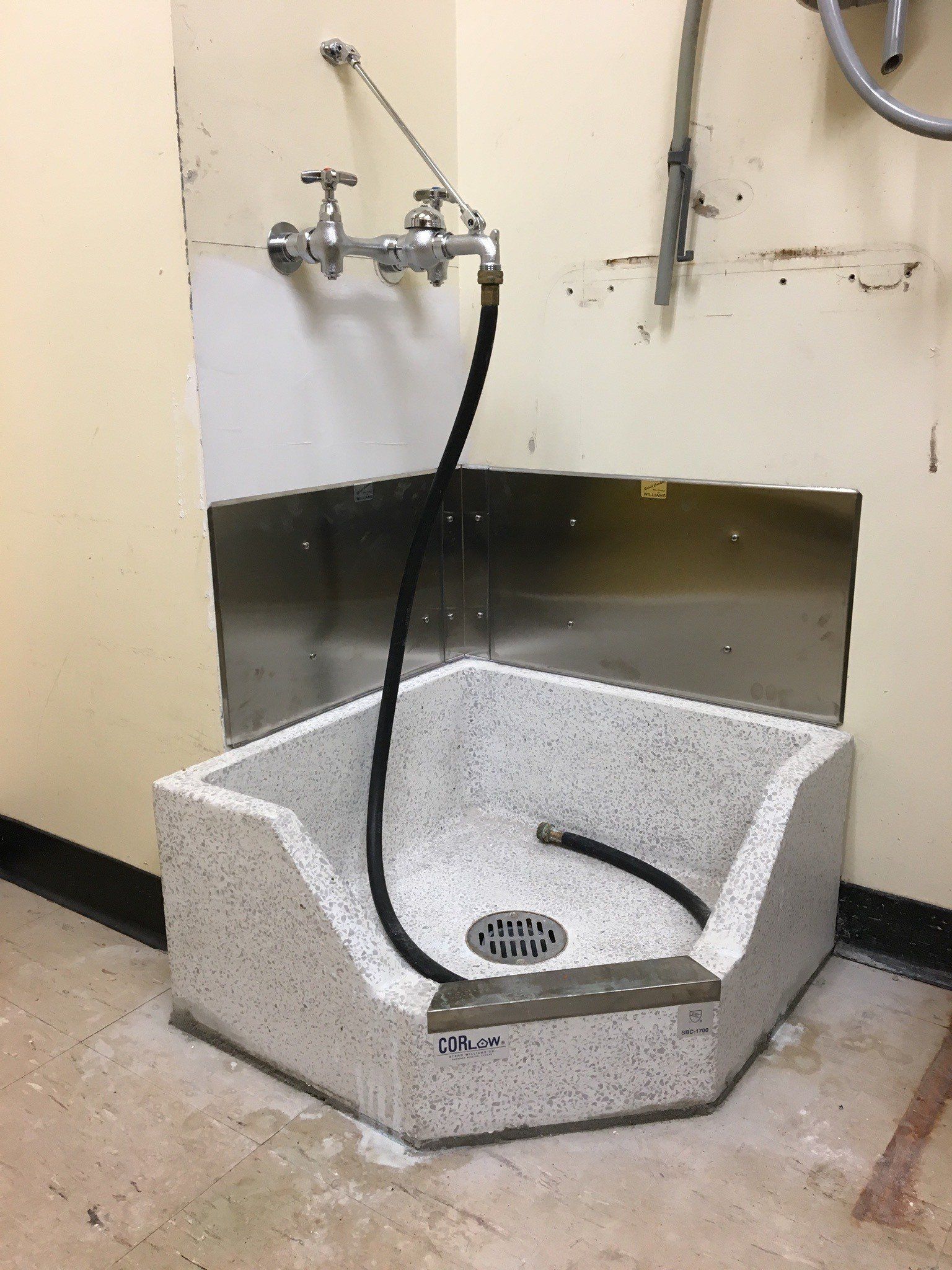 Corner utility sink with a faucet, sprayer hose, and wall-mounted backsplash.