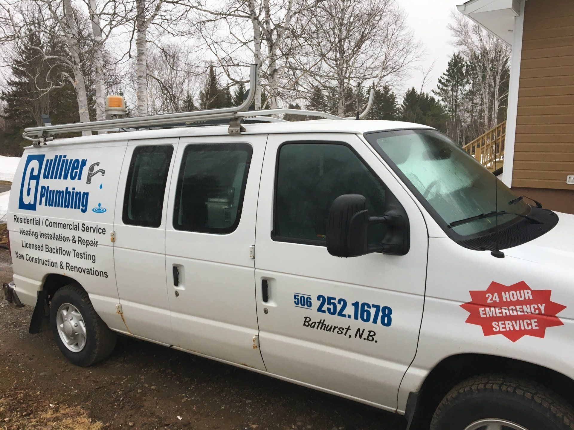 White plumbing service van parked outside a building. Text and logo on side. Roof rack holds a ladder.