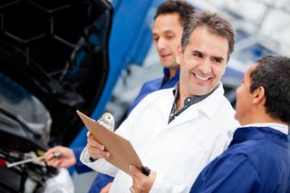 Car expert with a clipbpard takling to a mechanic