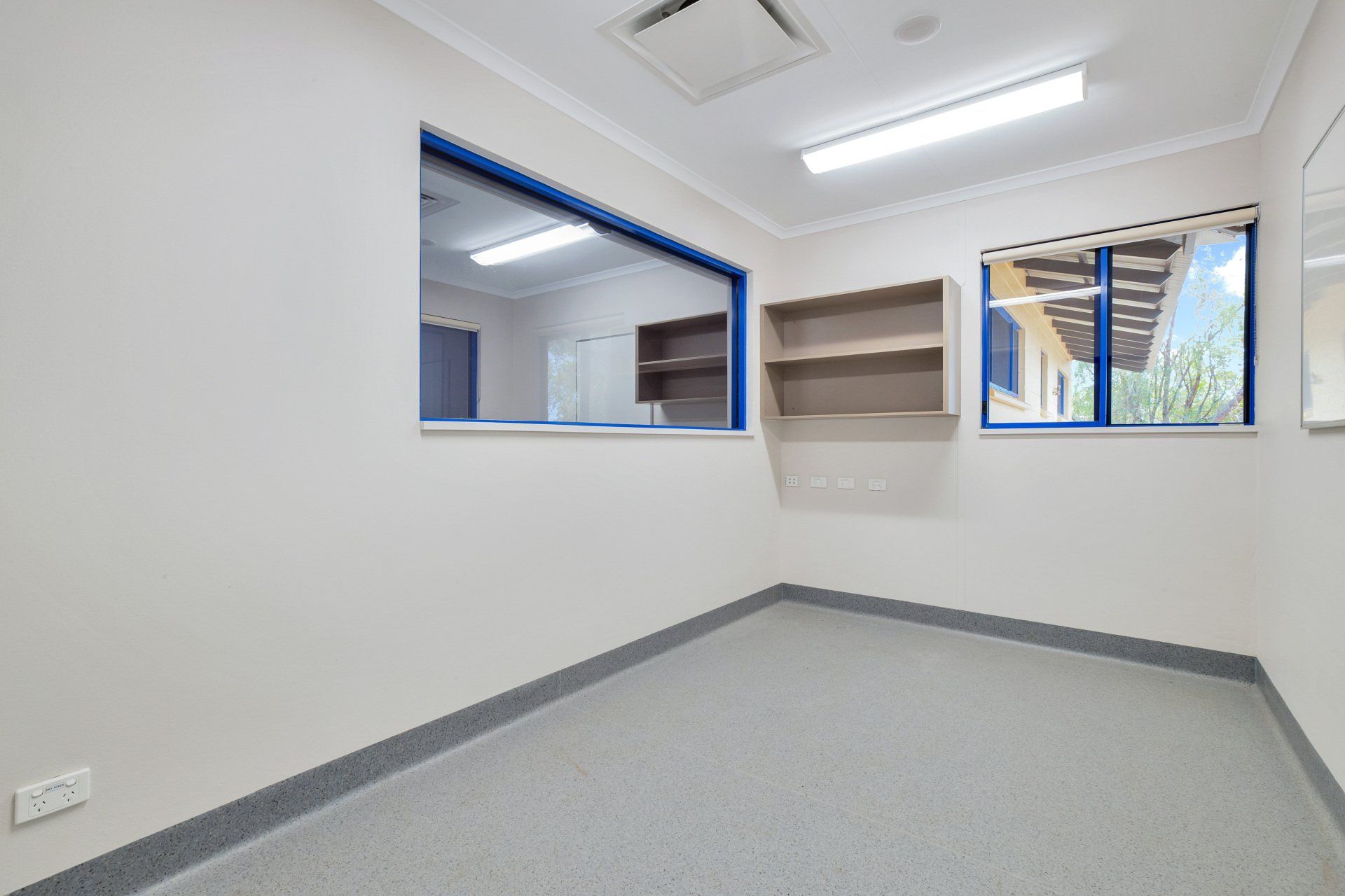 Empty room with gray floor, blue trim, and two windows. A shelf is mounted on the wall.