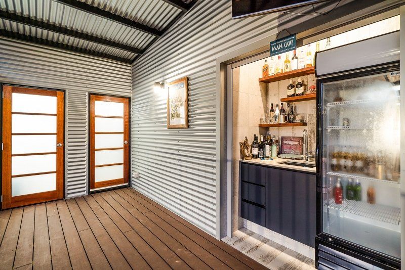 A rustic bar area with corrugated metal walls, wooden doors, and a refrigerator.