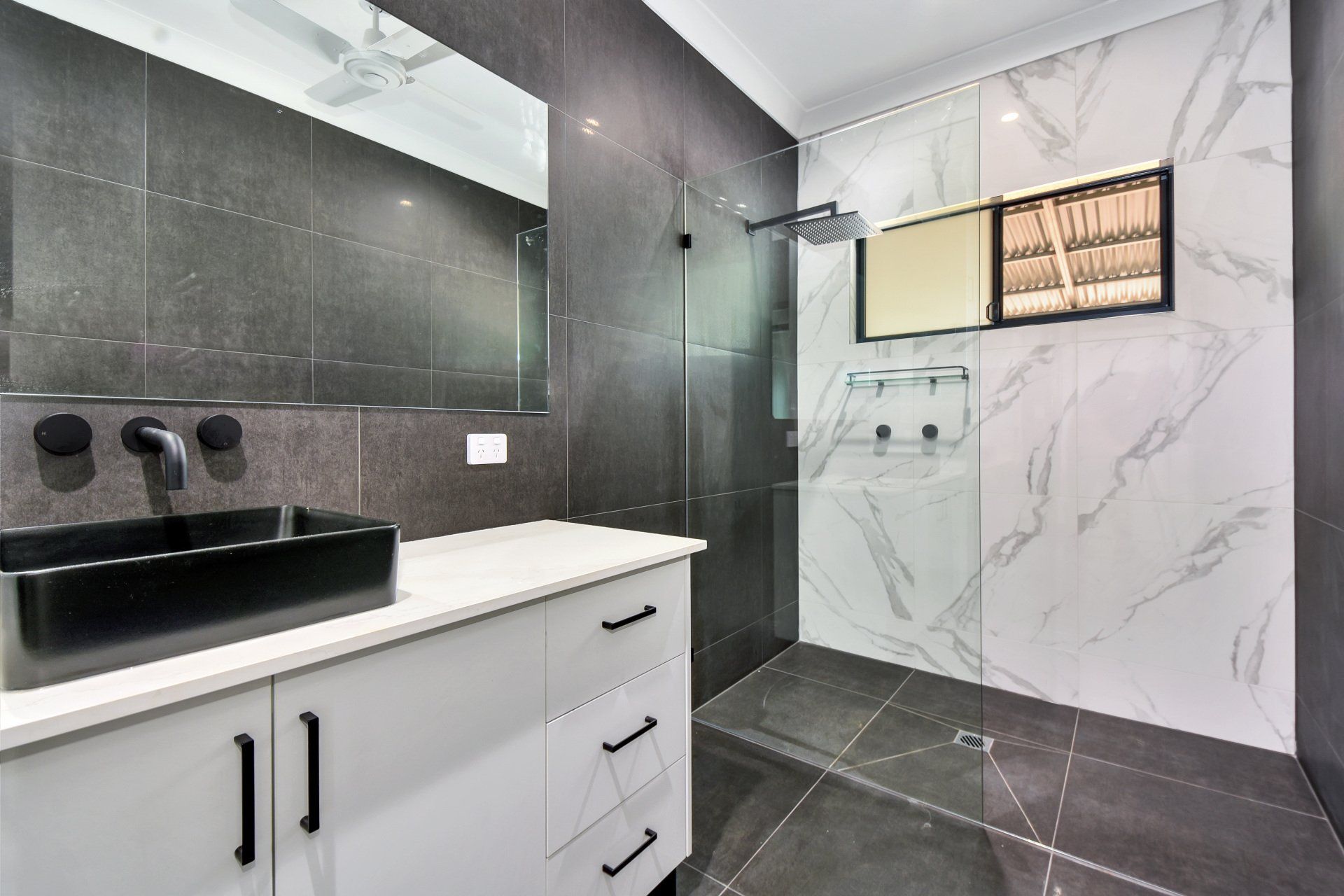 Bathroom with black sink, gray walls, white vanity, and marble tile shower.