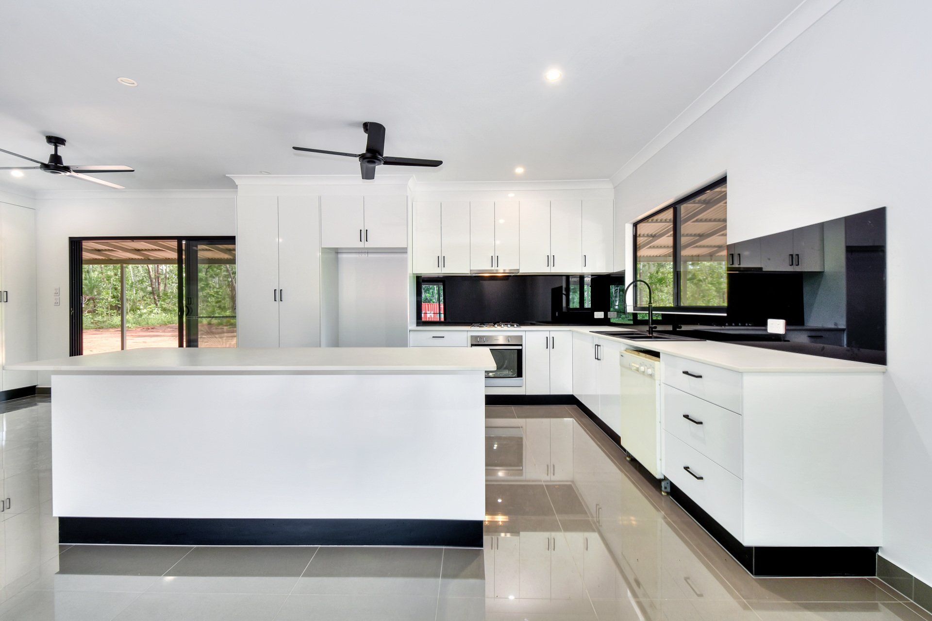 Modern white kitchen with island, cabinets, black accents, stainless steel appliances, and large windows.