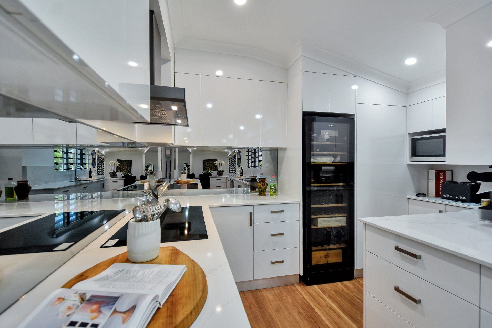 Modern white kitchen with black appliances and wood floors.