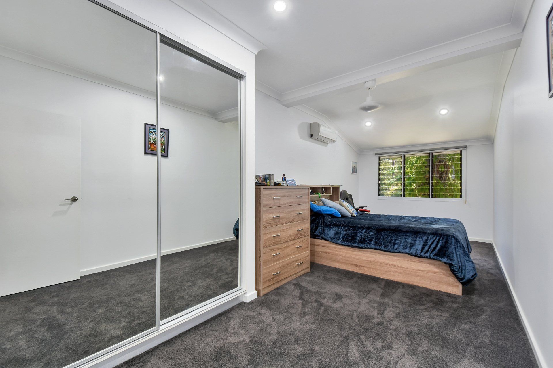 Bedroom with mirrored closet, gray carpet, bed with blue blanket, and a chest of drawers.