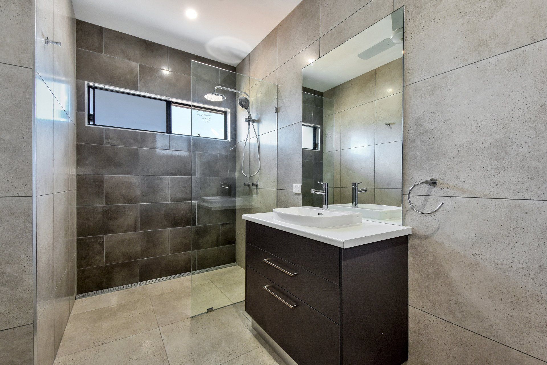 Modern bathroom with gray tiled walls, glass shower, vanity, and large mirror.