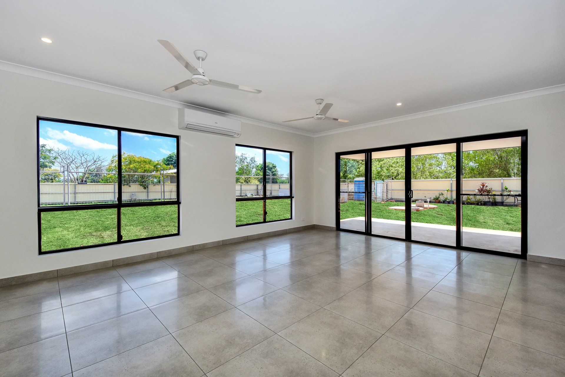 Empty room with large windows and sliding glass doors overlooking a green yard.