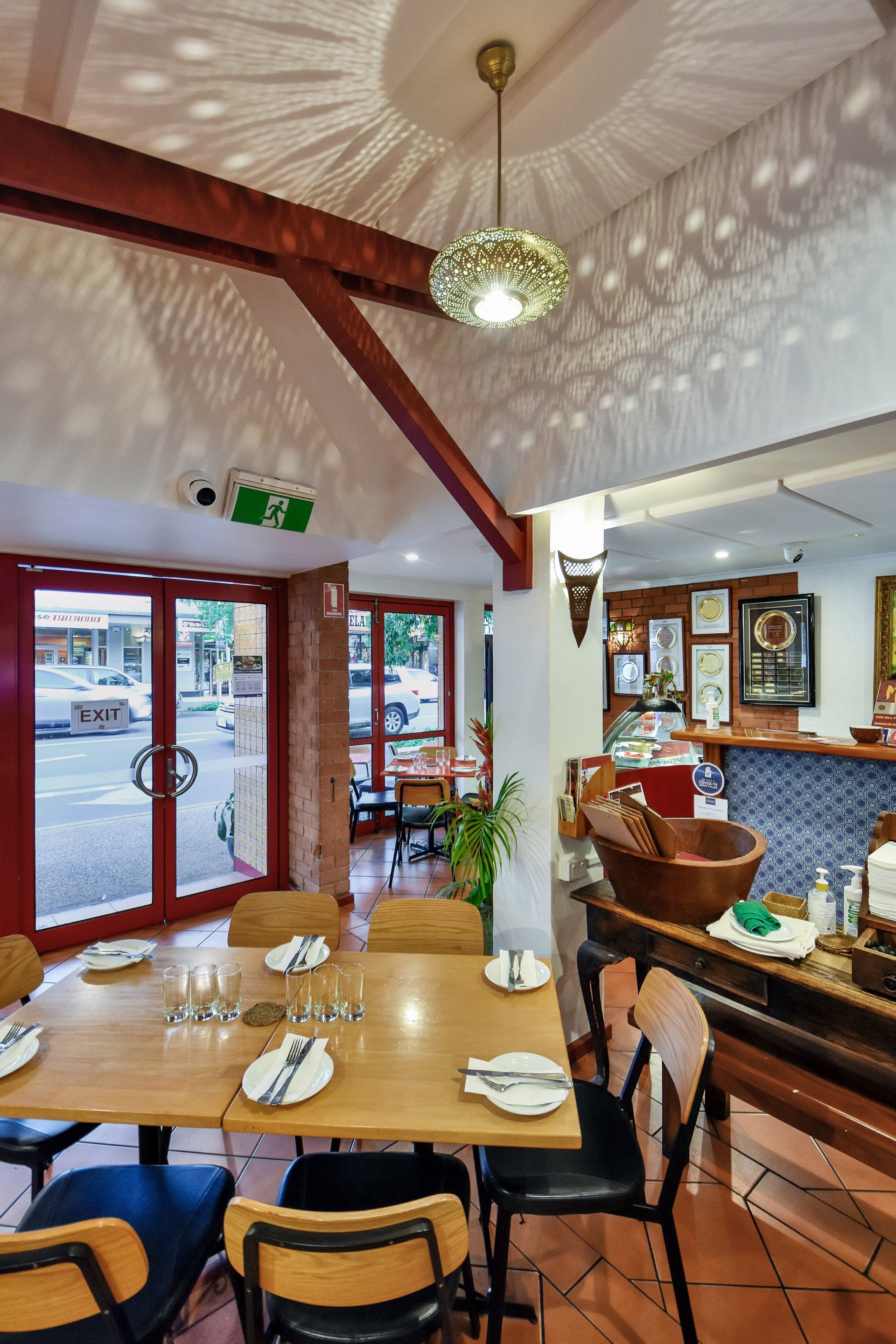 Restaurant interior with wooden tables, red trim, and a view of the street through open doors.