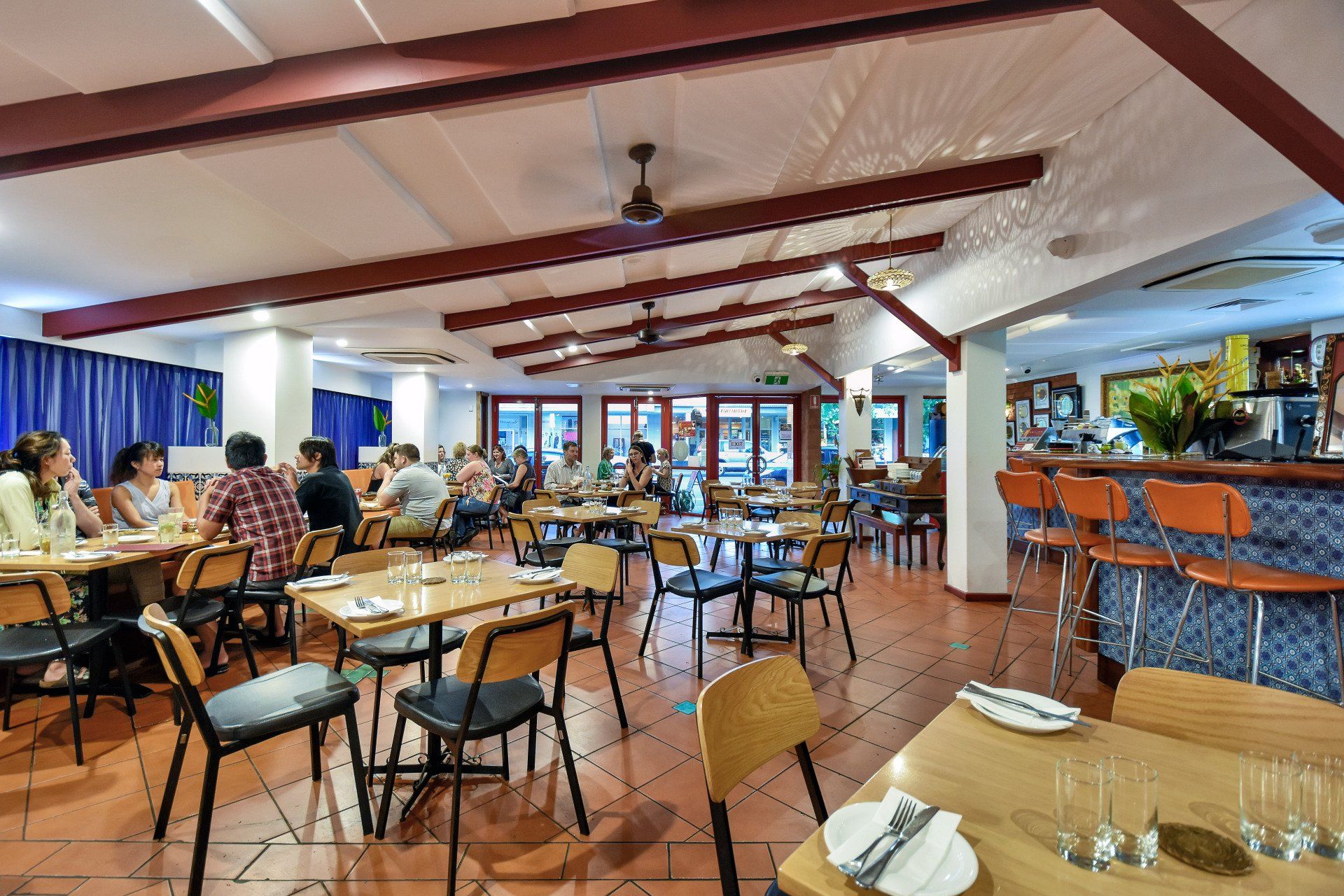 Restaurant interior with patrons seated at tables, bar with stools, and exposed beams.