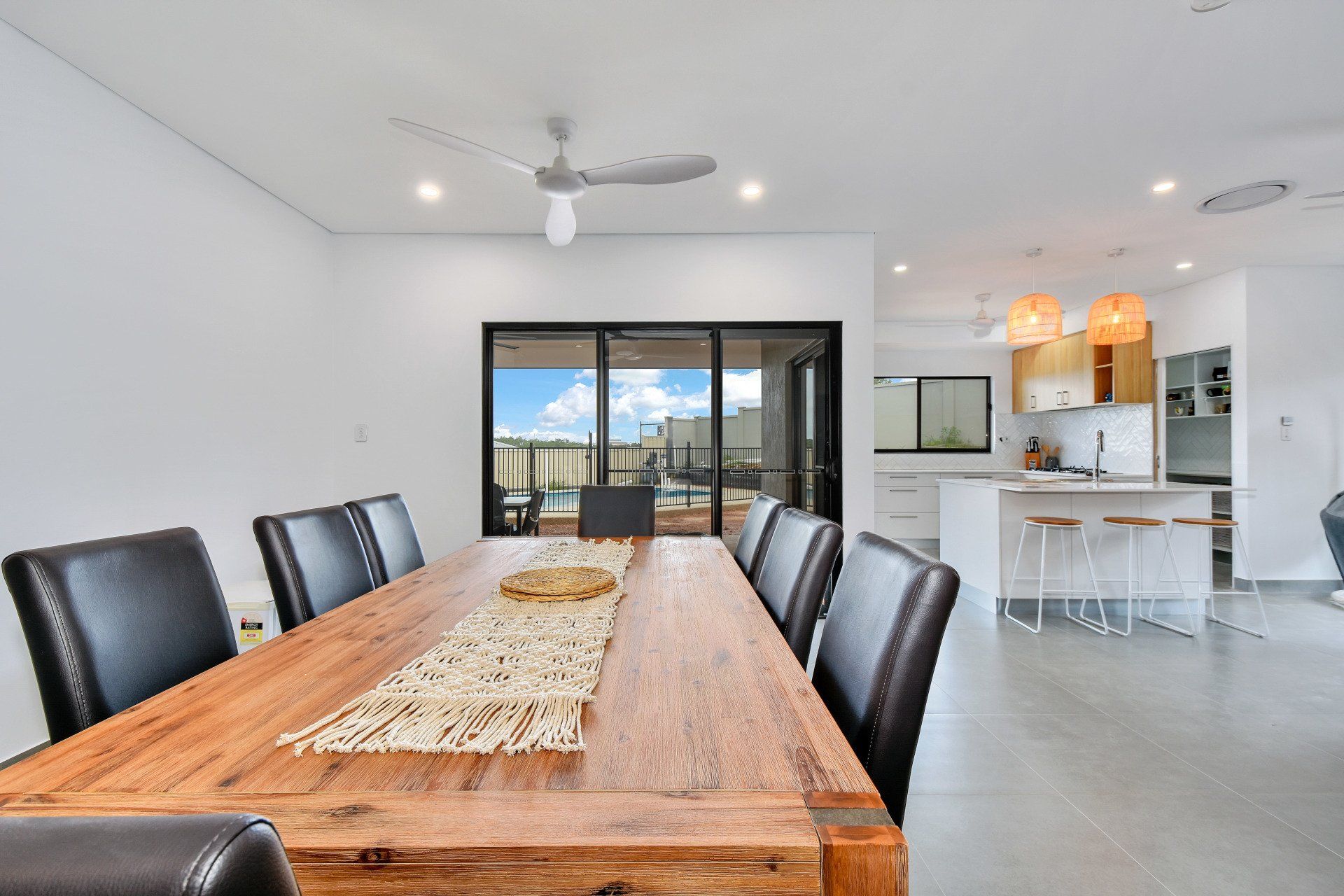 Dining room with wooden table and leather chairs, open to kitchen and outdoor view.