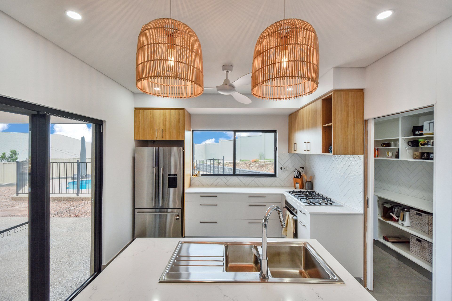 Modern kitchen with island and stainless steel appliances, featuring light wood cabinets and woven pendant lights.