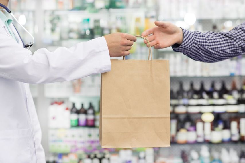 farmacista che dà prodotti acquistati in una busta di carta al cliente