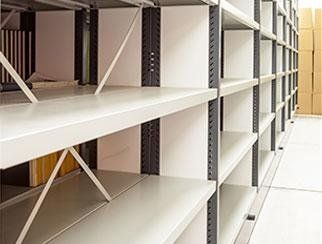In un magazzino, file di scaffalature metalliche industriali con superfici bianche e lisce e travi di supporto grigie.
