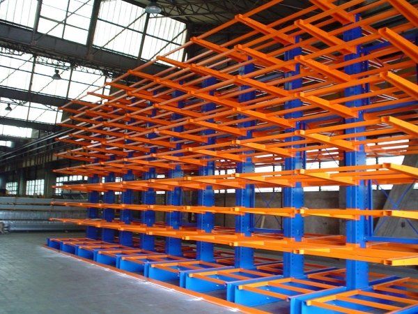 All'interno di un grande magazzino industriale, scaffalature a sbalzo vuote in acciaio blu con bracci arancioni, disposte in file.