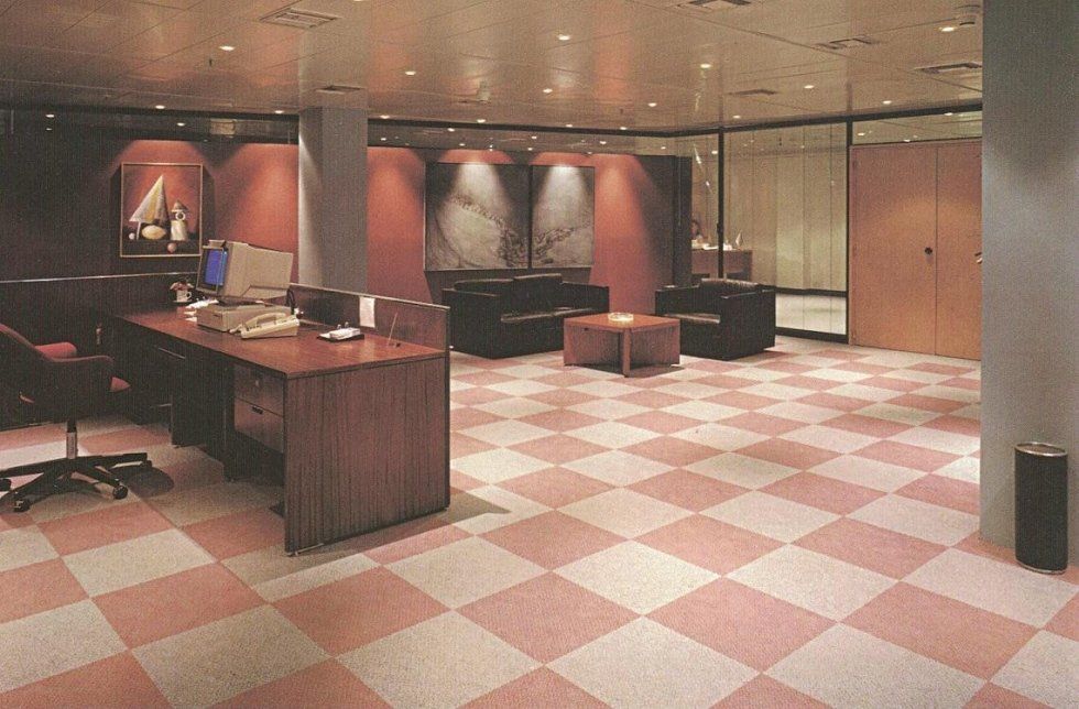 Una sala d'attesa in ufficio con pavimento a scacchi rosa e beige, scrivania in legno, sedie nere e opere d'arte moderne alle pareti.