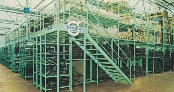 Un sistema di scaffalature industriali a più livelli in un magazzino, con il logo Volvo ben visibile su una scala in acciaio color verde acqua.