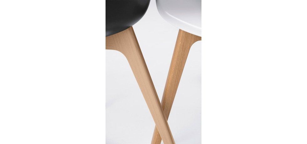 Primo piano delle gambe in legno di una sedia nera e di una sedia bianca che si incrociano su uno sfondo neutro.