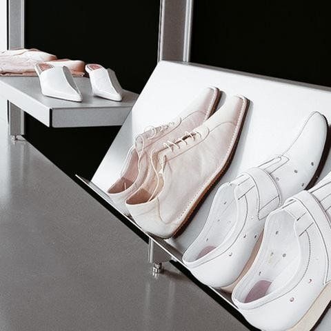 Un allestimento minimalista per la vendita al dettaglio, con paia di scarpe in pelle bianca disposte su eleganti scaffali inclinati su uno sfondo nero.