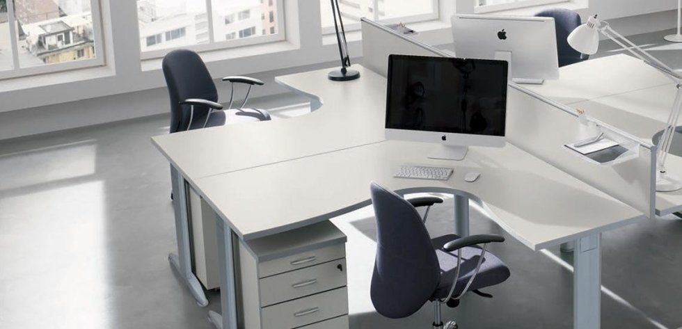 Un moderno spazio di lavoro in ufficio con scrivanie angolari bianche, sedie ergonomiche grigie, monitor per computer e schedari.
