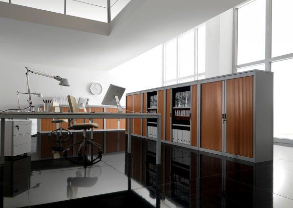 Interno di un ufficio moderno con scrivania, sedia e armadi alti con pannelli in legno su un pavimento nero lucido.