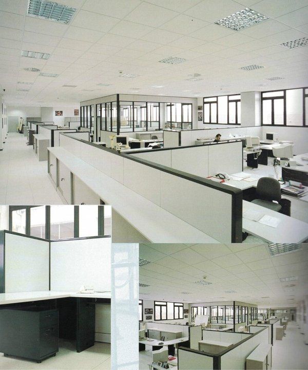 Immagine composita di un moderno ufficio open space con scrivanie a cubicolo bianche, arredamento neutro e ampie finestre.