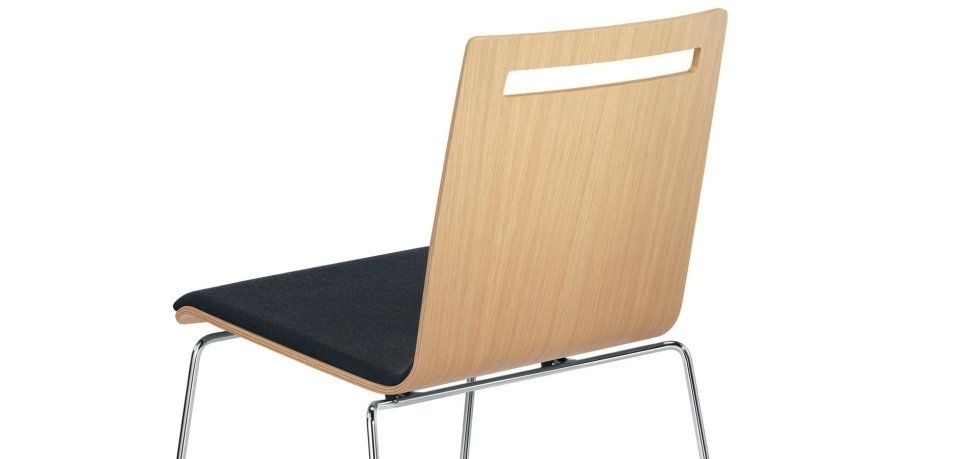 Una sedia moderna con schienale in legno chiaro caratterizzato da un incavo a forma di maniglia, seduta imbottita scura e gambe sottili in metallo.