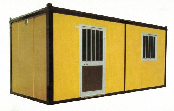Un'unità modulare prefabbricata di colore giallo con porta e finestra piccole di colore bianco, entrambe dotate di inferriate di sicurezza verticali.