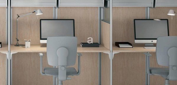 Due moderne postazioni di lavoro con computer, lampade da scrivania e sedie grigie in un ambiente ufficio con pareti rivestite in legno chiaro.
