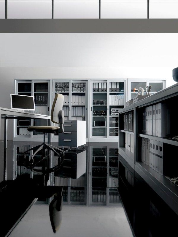 Un ufficio moderno e minimalista con schedari bianchi, una scrivania con computer e una sedia su un pavimento nero lucido.