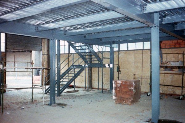 All'interno di un magazzino è in costruzione un soppalco in acciaio con scala metallica.