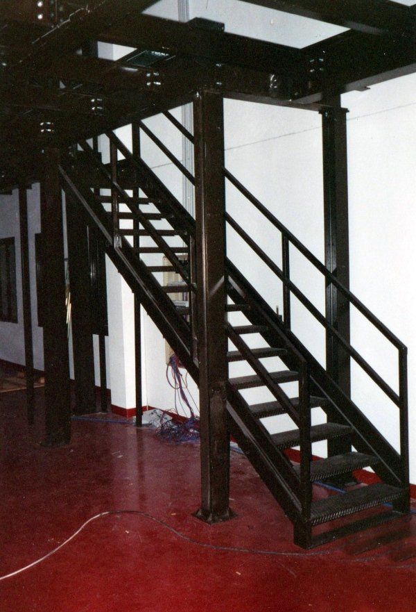 Una scala in metallo nero con corrimano in una stanza con pavimento rosso lucido e pareti bianche.