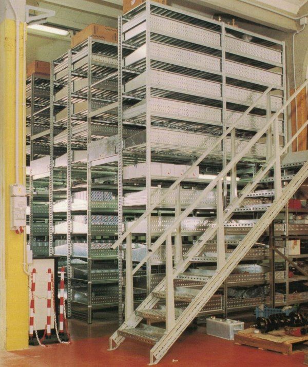 Una scaffalatura metallica a più livelli all'interno di un magazzino industriale, accessibile tramite una scala metallica.