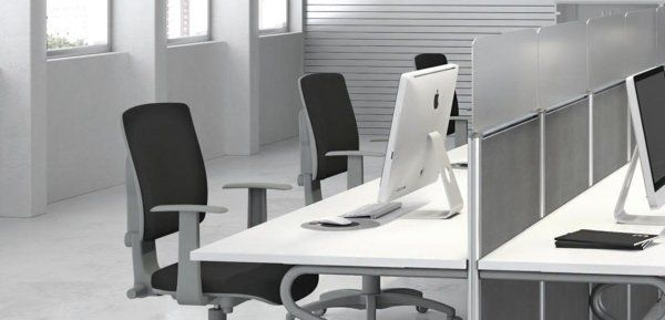 Moderno spazio di lavoro in ufficio con file di scrivanie, sedie nere e computer sullo sfondo di finestre.