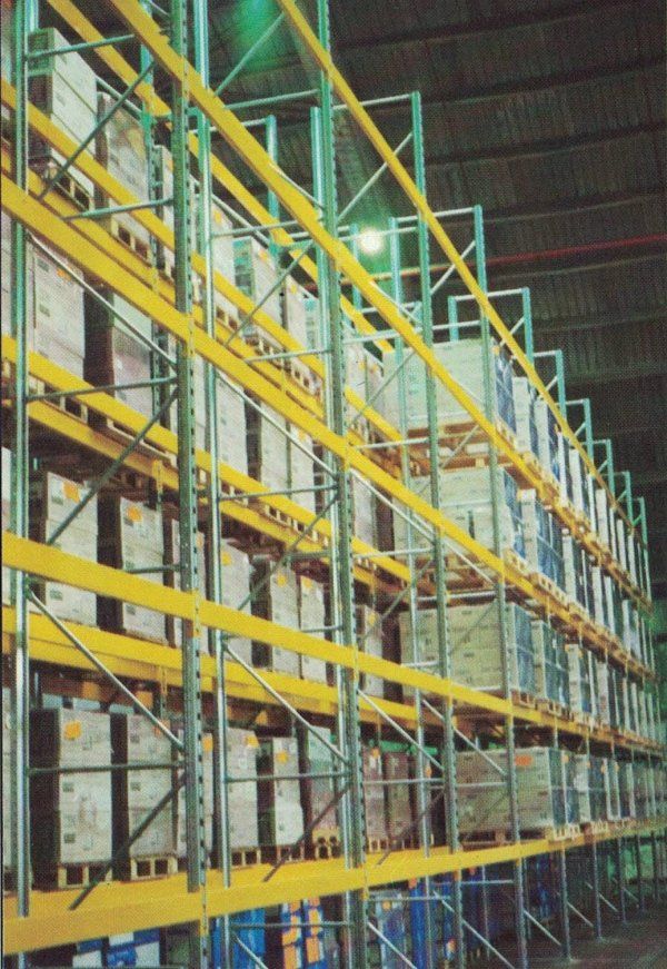 Magazzino industriale con scaffalature metalliche alte, su cui sono impilati pallet di merci, visto da un'angolazione bassa.