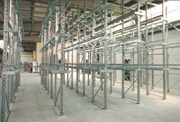Una fila di alte scaffalature metalliche industriali vuote all'interno di un magazzino con pavimento in cemento.