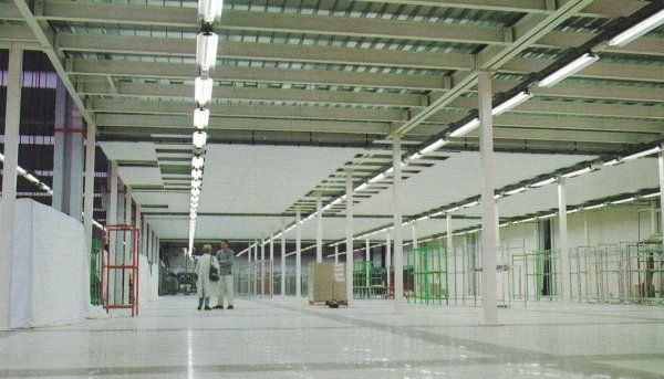 Due persone si trovano in un grande magazzino minimalista con pavimento bianco, colonne bianche e lunghe file di lampade a soffitto.