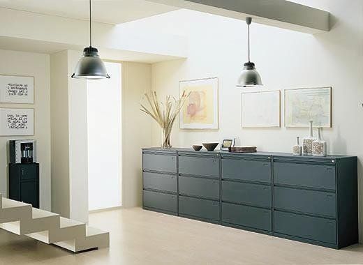 Un moderno interno d'ufficio caratterizzato da un lungo schedario laterale grigio scuro addossato a una parete con quadri incorniciati.