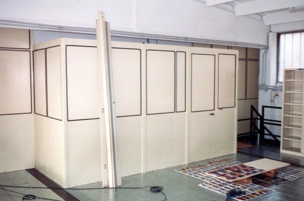 Interno di un ufficio con pareti divisorie modulari color bianco sporco e un lungo pannello appoggiato ad esse, su un pavimento chiaro.