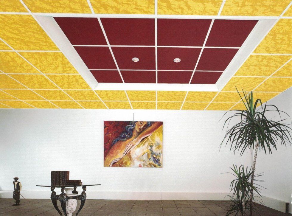 Interno di una stanza con controsoffitto rivestito di piastrelle gialle a rilievo e un quadrato centrale di piastrelle rosso scuro.