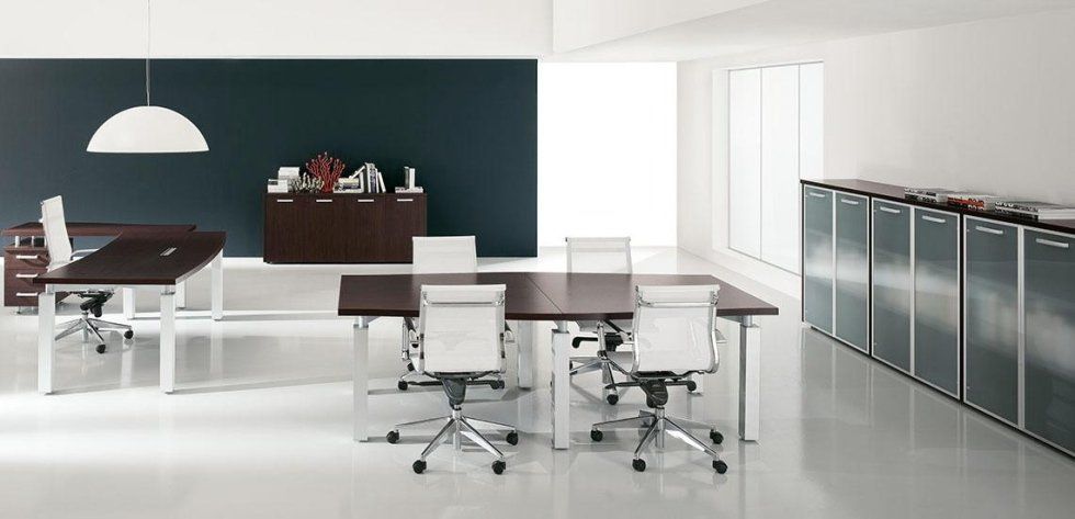 Moderno spazio di lavoro in ufficio con scrivanie in legno scuro, sedie bianche, una lampada a sospensione e una fila di armadietti con ante in vetro.