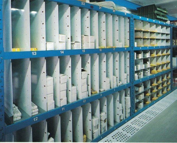 Una scaffalatura metallica blu in un magazzino, piena di divisori verticali ben organizzati che contengono scatole e materiali di vario genere.