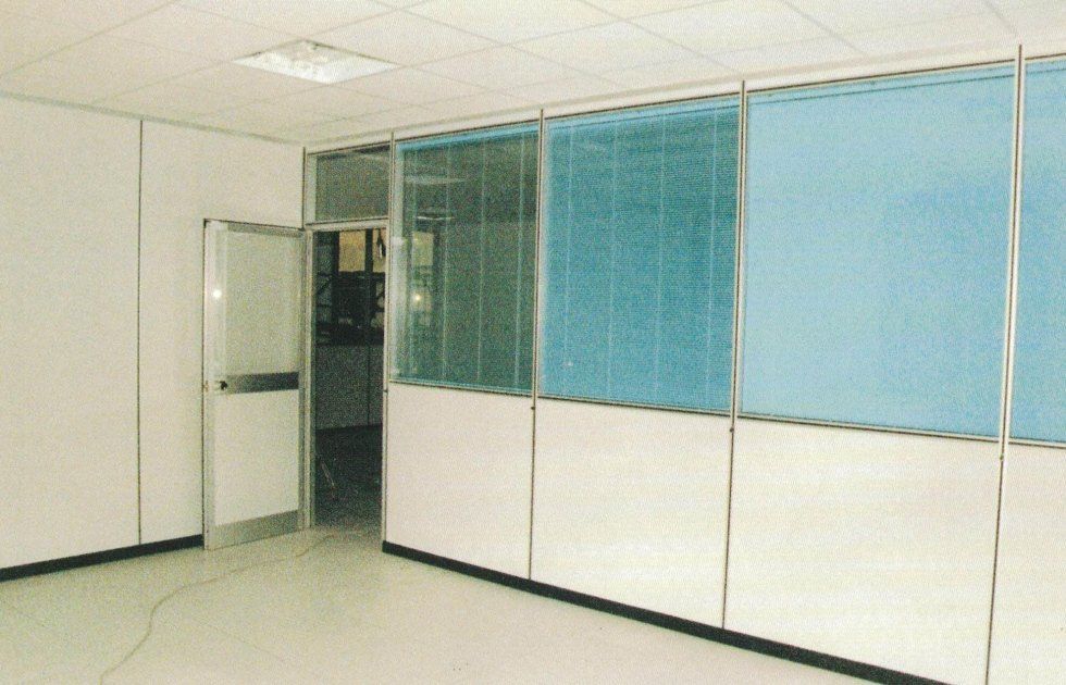 Un ufficio interno con porta bianca, pareti divisorie in vetro e pannelli bianchi su uno sfondo neutro di pavimento e soffitto.