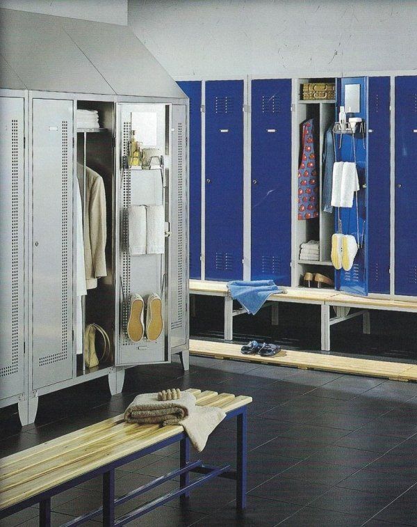 Una fila di armadietti blu e argento in uno spogliatoio con panche di legno e scarpe sul pavimento scuro.