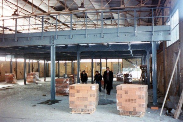 Un interno industriale con un soppalco in acciaio rialzato e due pile di mattoni su pallet di legno in primo piano.
