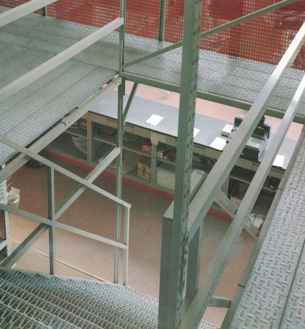 Una vista da un soppalco metallico che inquadra un livello inferiore con scaffalature industriali e una zona scrivania.