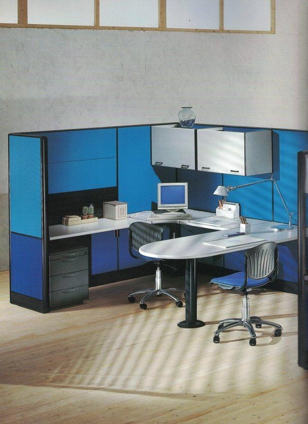 Un cubicolo d'ufficio blu con scrivania bianca, armadietti e due sedie su un pavimento in legno.