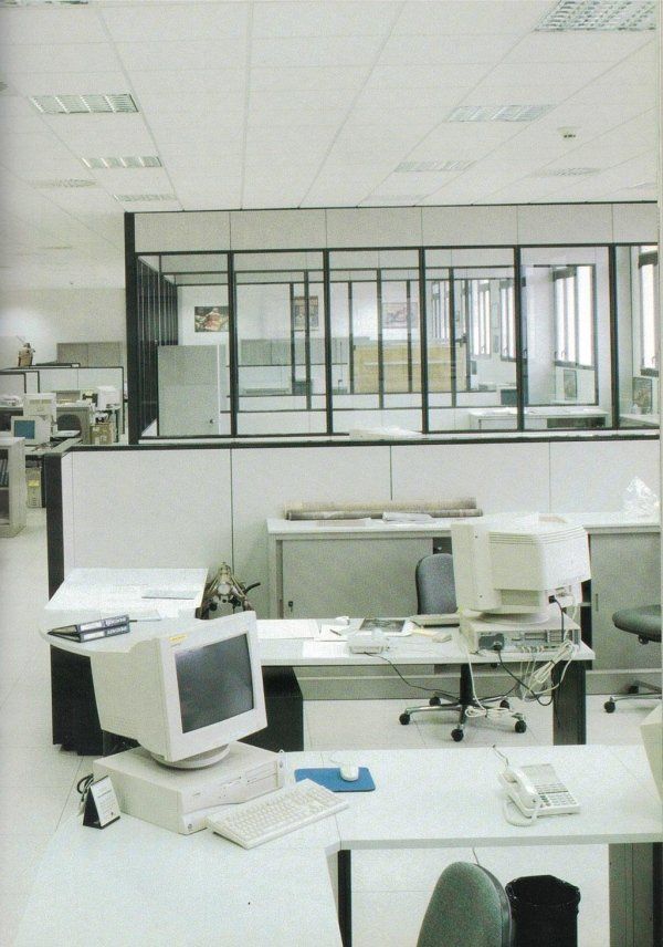 Un ufficio tranquillo e luminoso con postazioni di lavoro individuali dotate di computer desktop vintage e pareti in vetro.